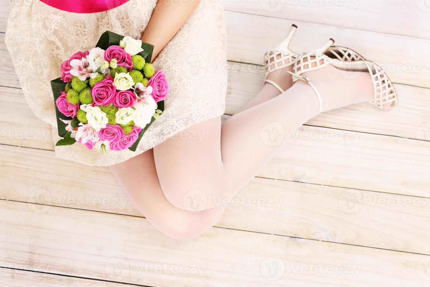 Bride's legs and flowers on wooden floor photo