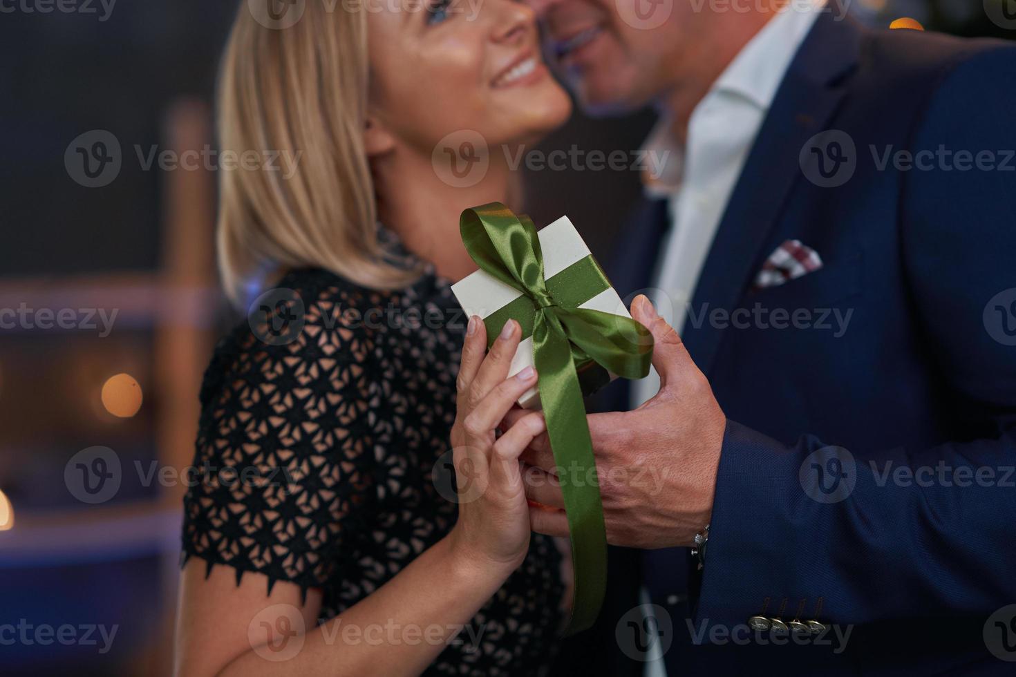 Couple kiss in front of chrismas tree holding gift photo