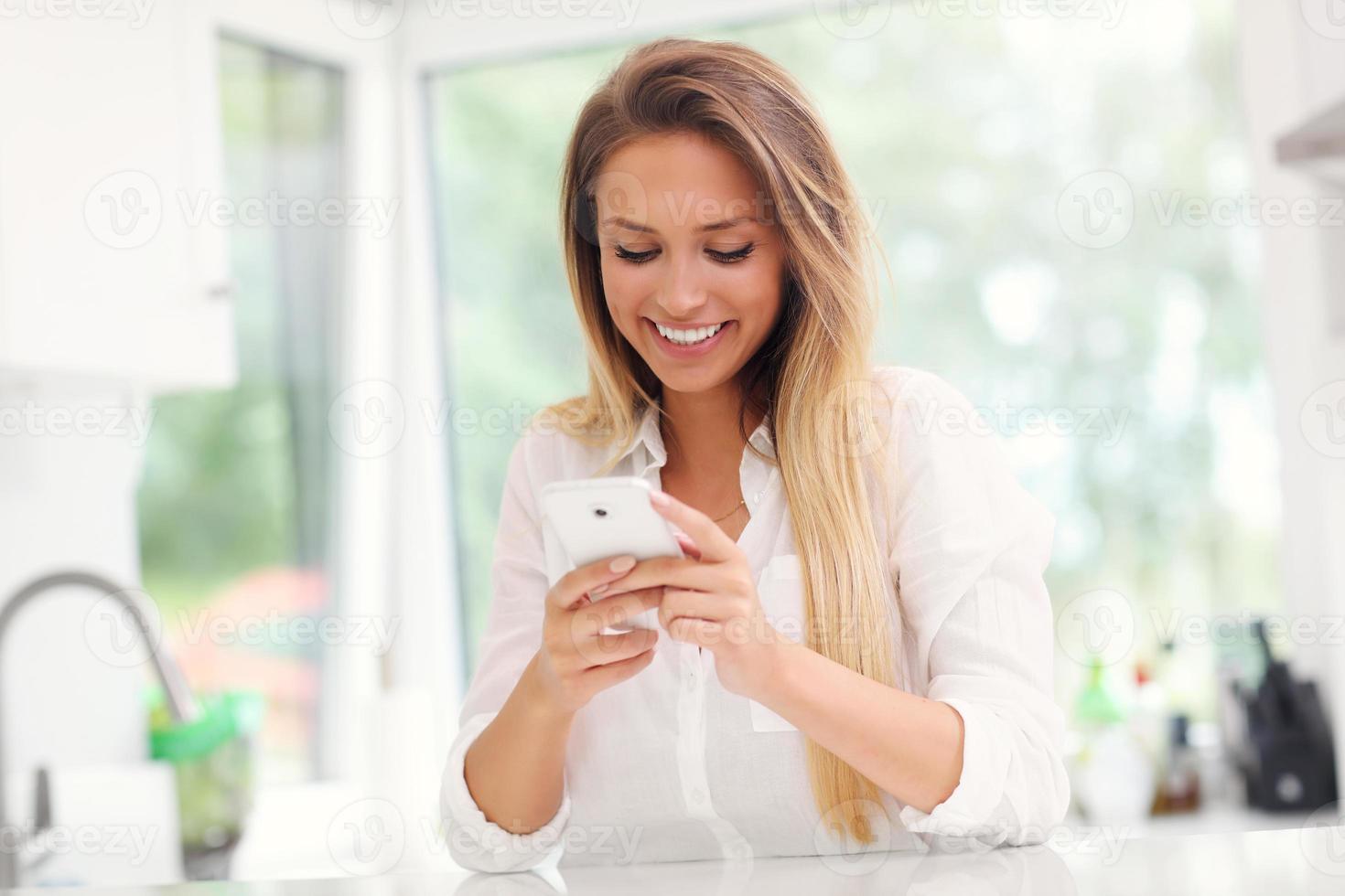 Young woman with smartphone in kitchen photo