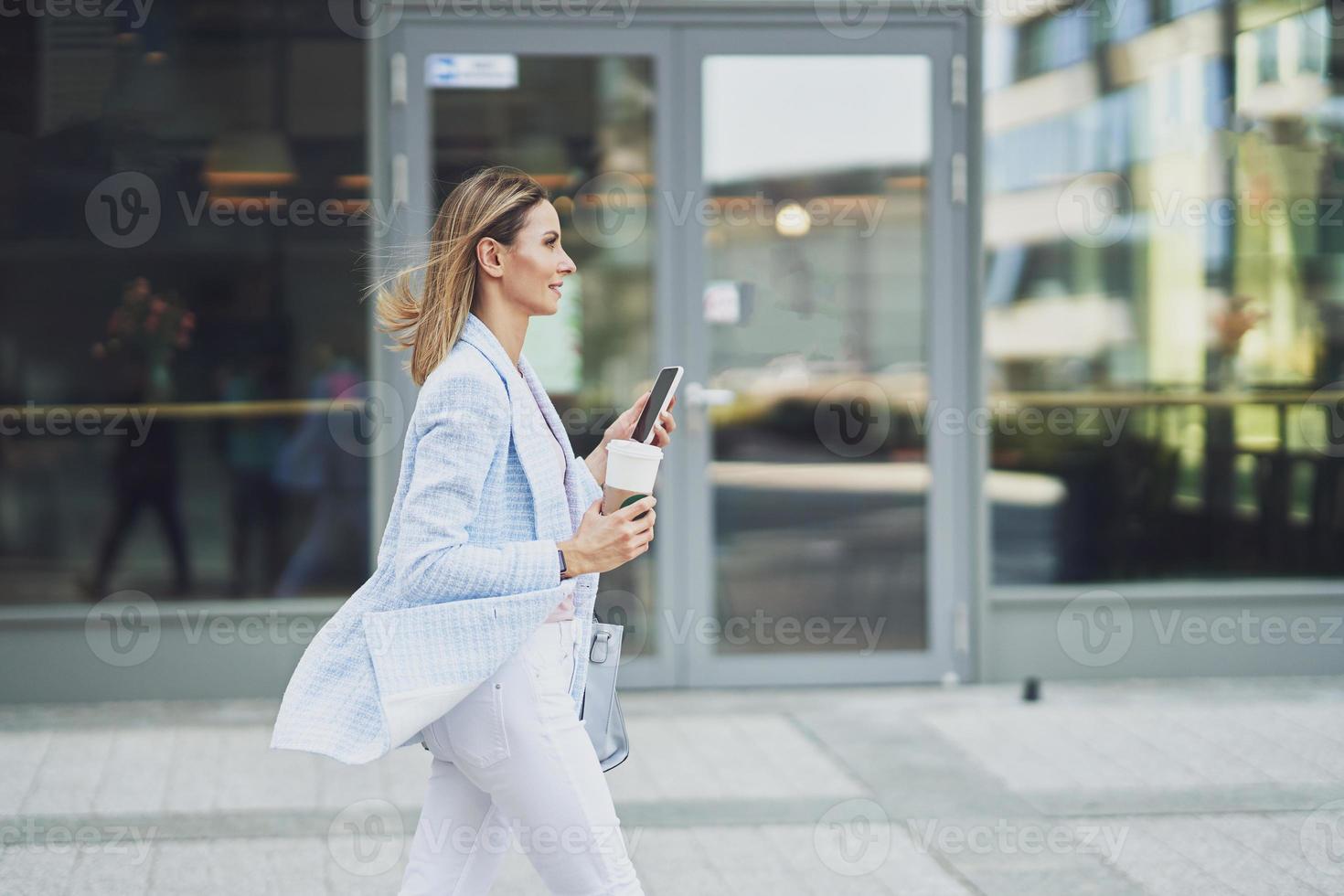Adult attractive woman with smartphone walking in the city photo