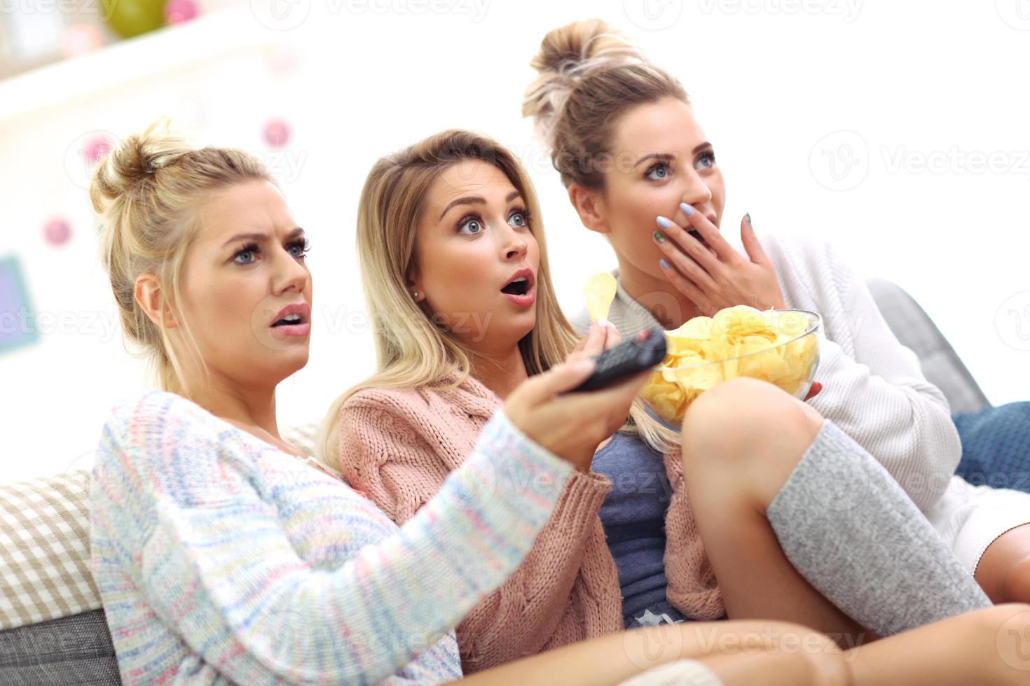 Three beautiful young women watching tv at home photo