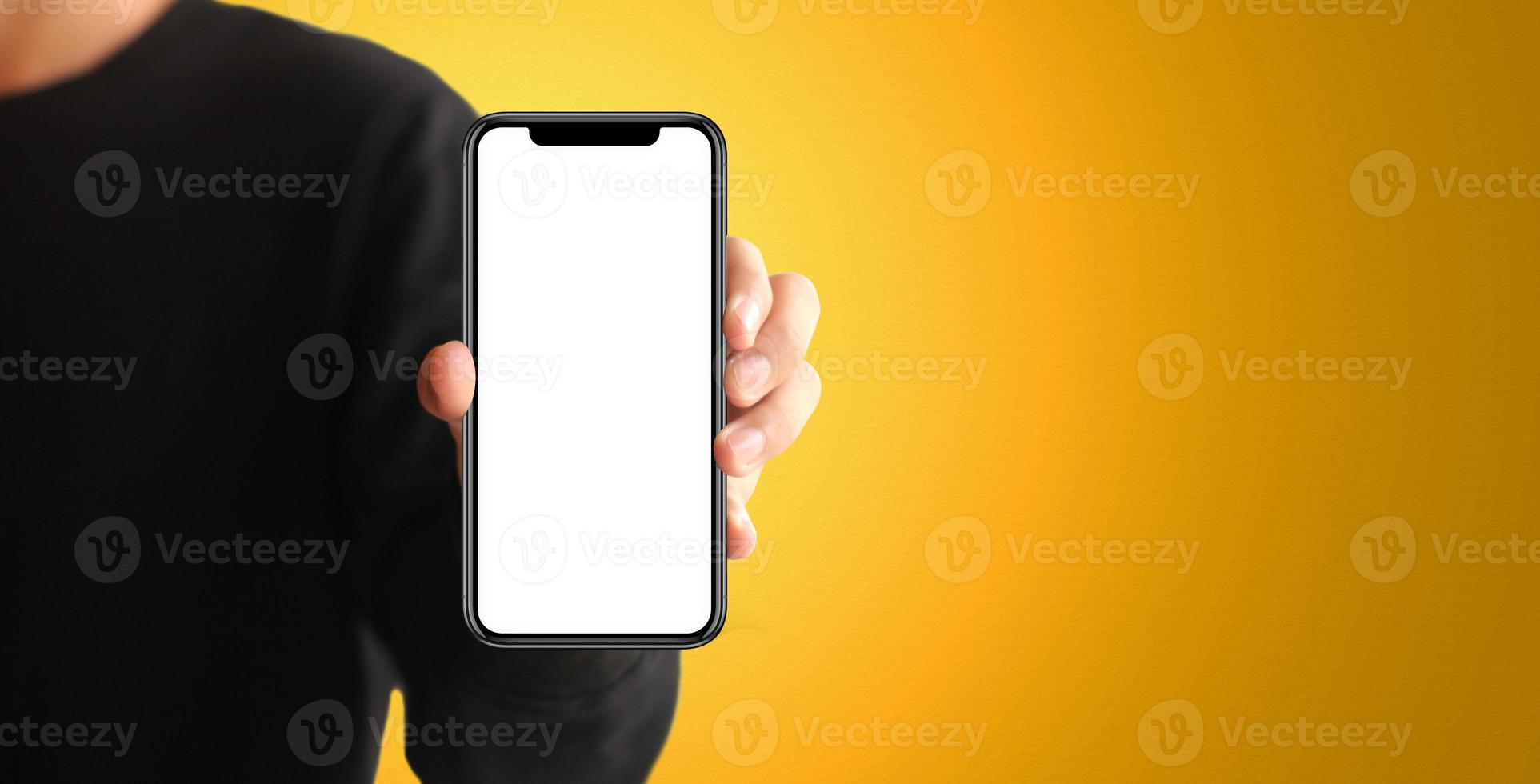 Hand holding the black smartphone with blank screen on yellow colour background photo