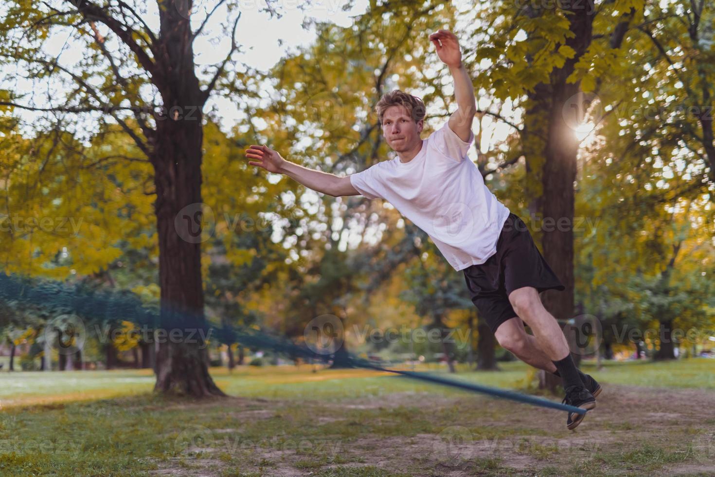 Young man balancing and jumping on slackline. Man walking, jumping and balancing on rope in park. photo