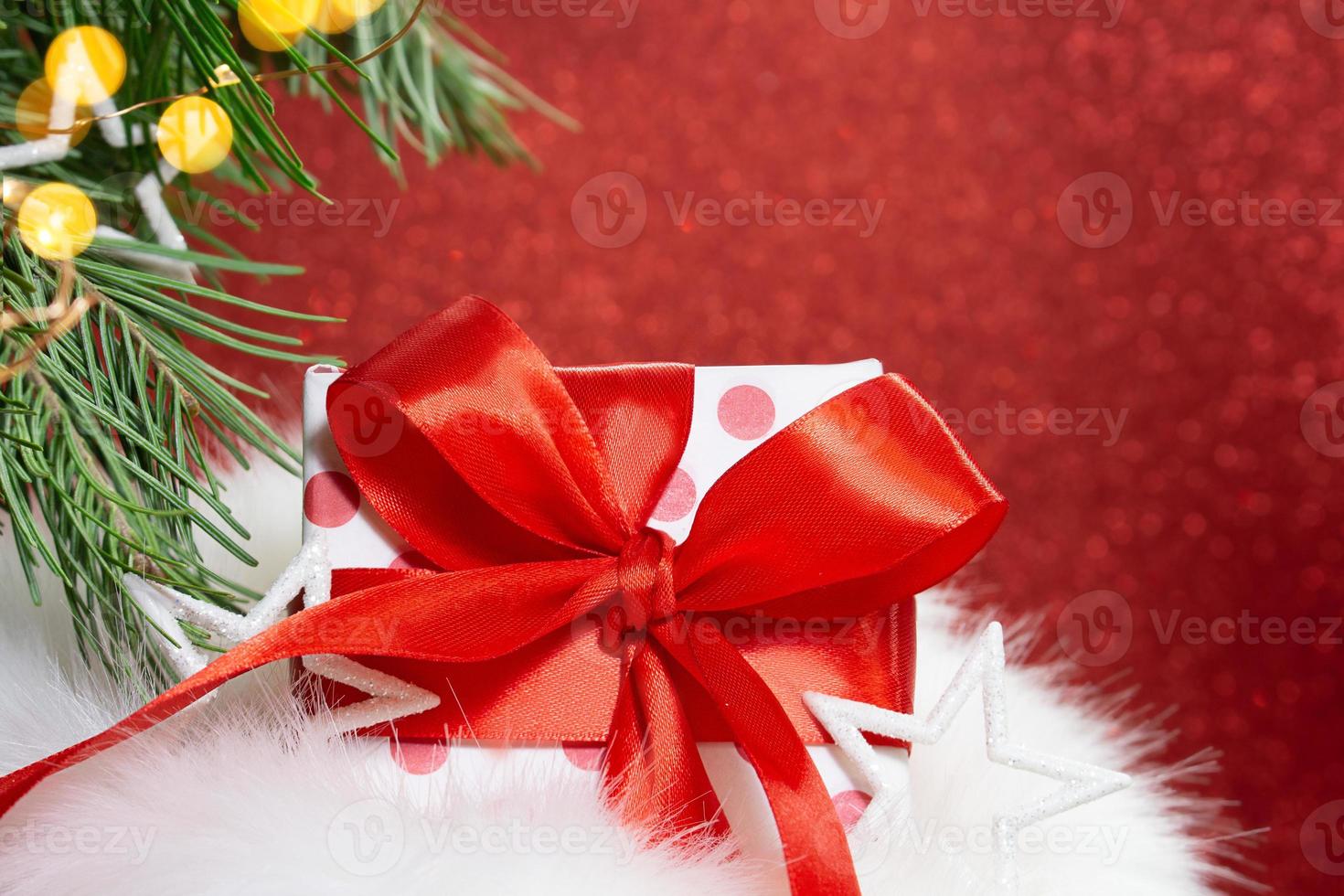 Fur bag and gift box with polka dot and bow with spruce branches and bokeh on red shiny background. Christmas, New Year. Copy space photo