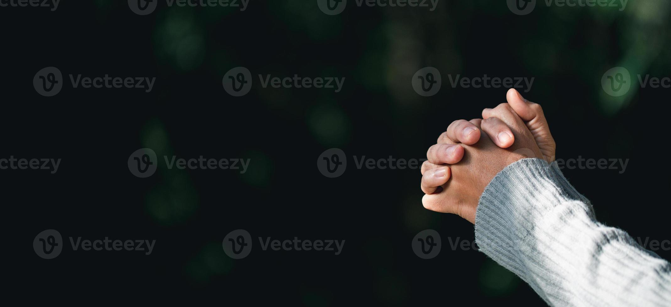 mano de persona de oración en fondo negro. la mujer católica cristiana está rezando a dios en la oscuridad en la iglesia. chica cree y fe en jesucristo. la religión de cristo y el cristianismo adoran o rezan concepto. foto