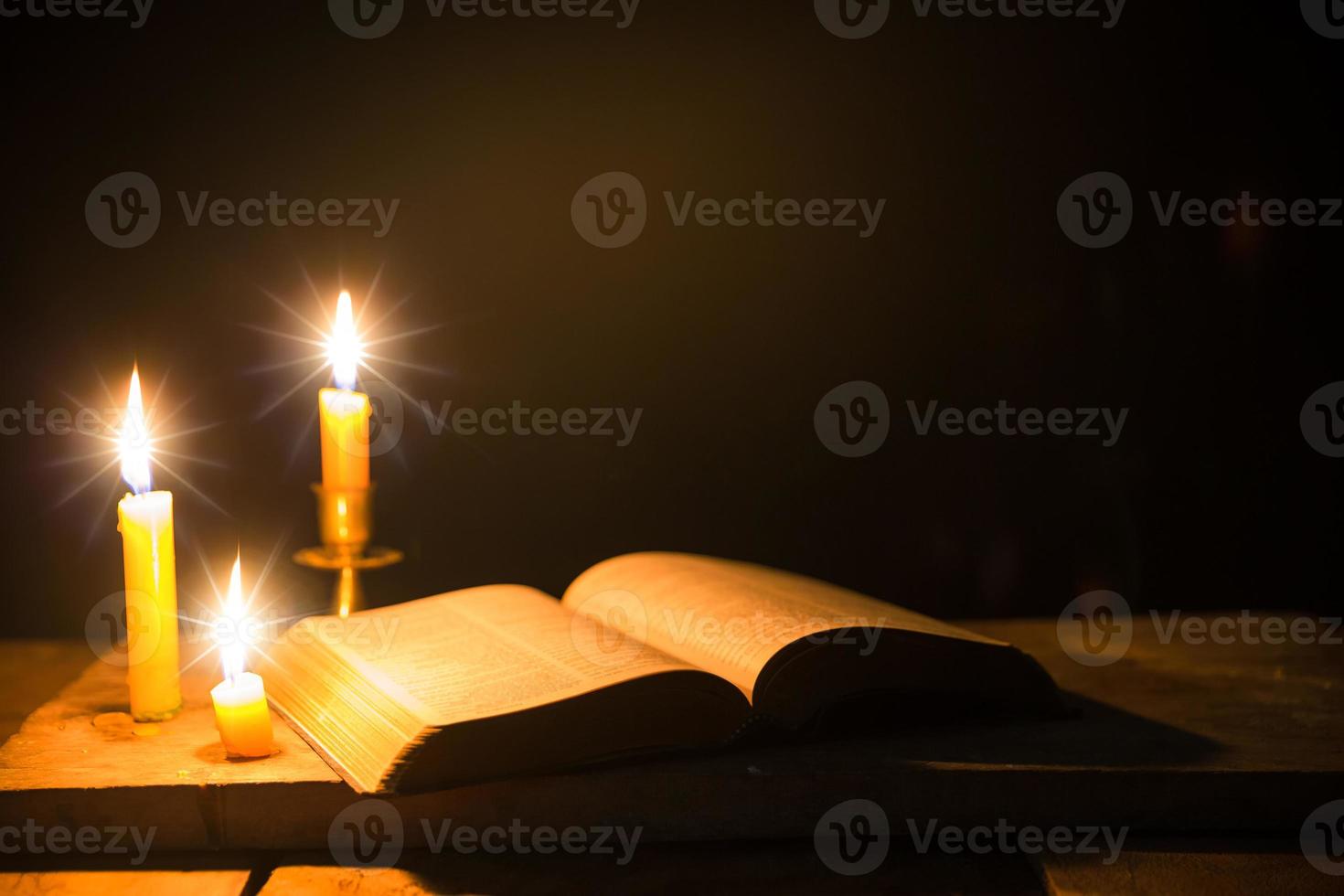 velas encendidas con la sagrada biblia y la cruz o el crucifijo sobre un fondo de madera antiguo en la iglesia. luz de las velas y libro abierto sobre una mesa de madera vintage estudio y lectura del cristianismo en el hogar. concepto de la religión de cristo foto