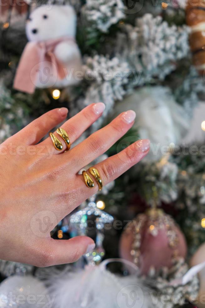 Girl hand wearing golden rings with a Christmas Tree in the background. Festive Christmas and gift giving concepts. photo