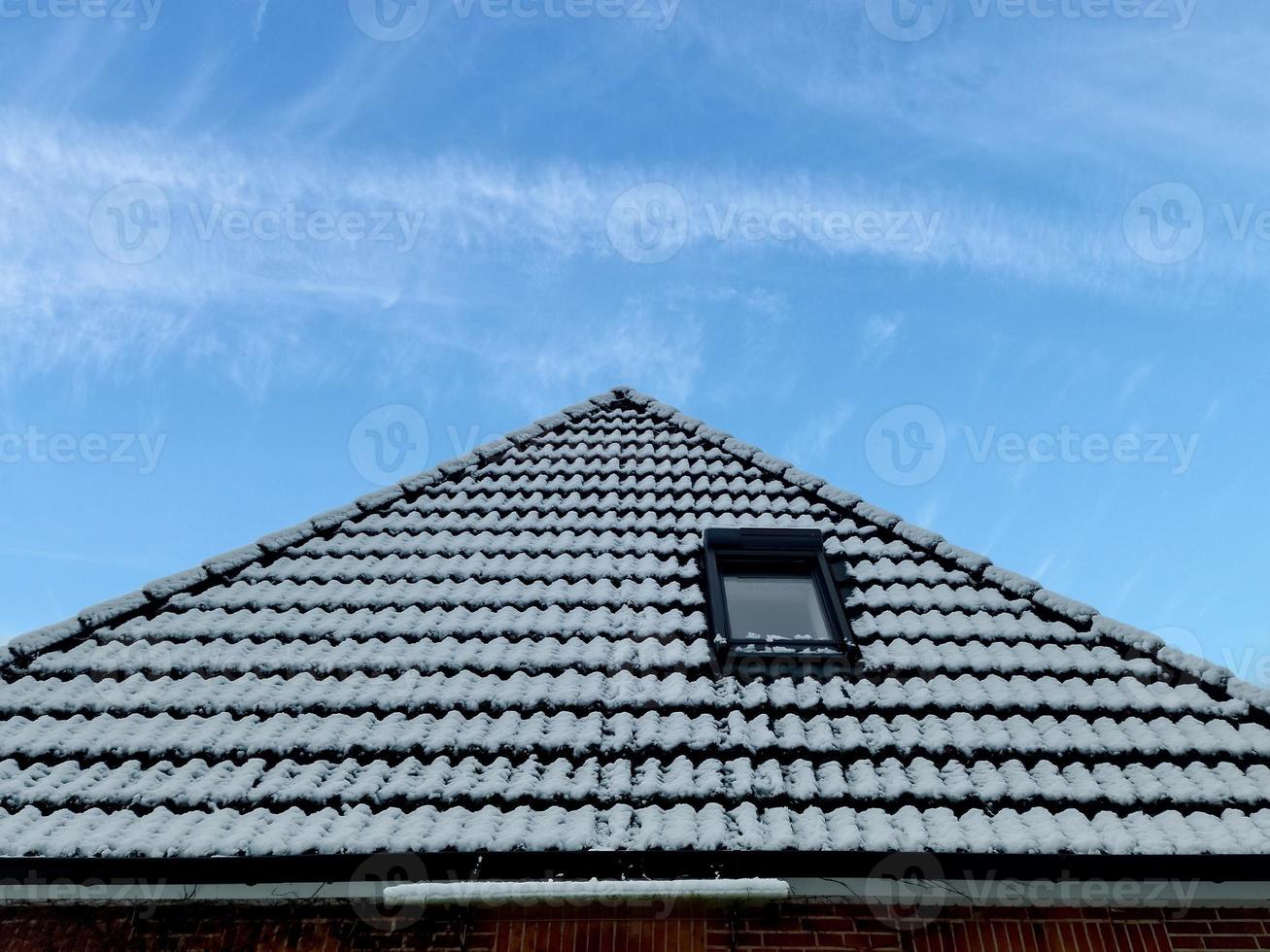 Open roof window in velux style with black roof tiles covered in snow during winter photo