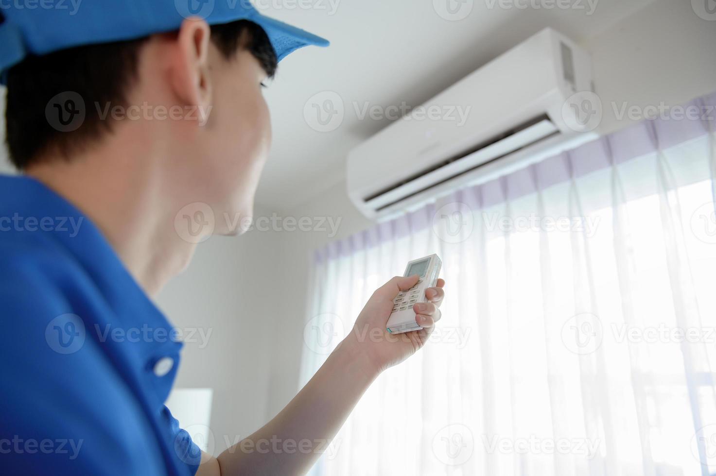 An Asian young Technician service man wearing blue uniform checking ,  cleaning air conditioner in home photo