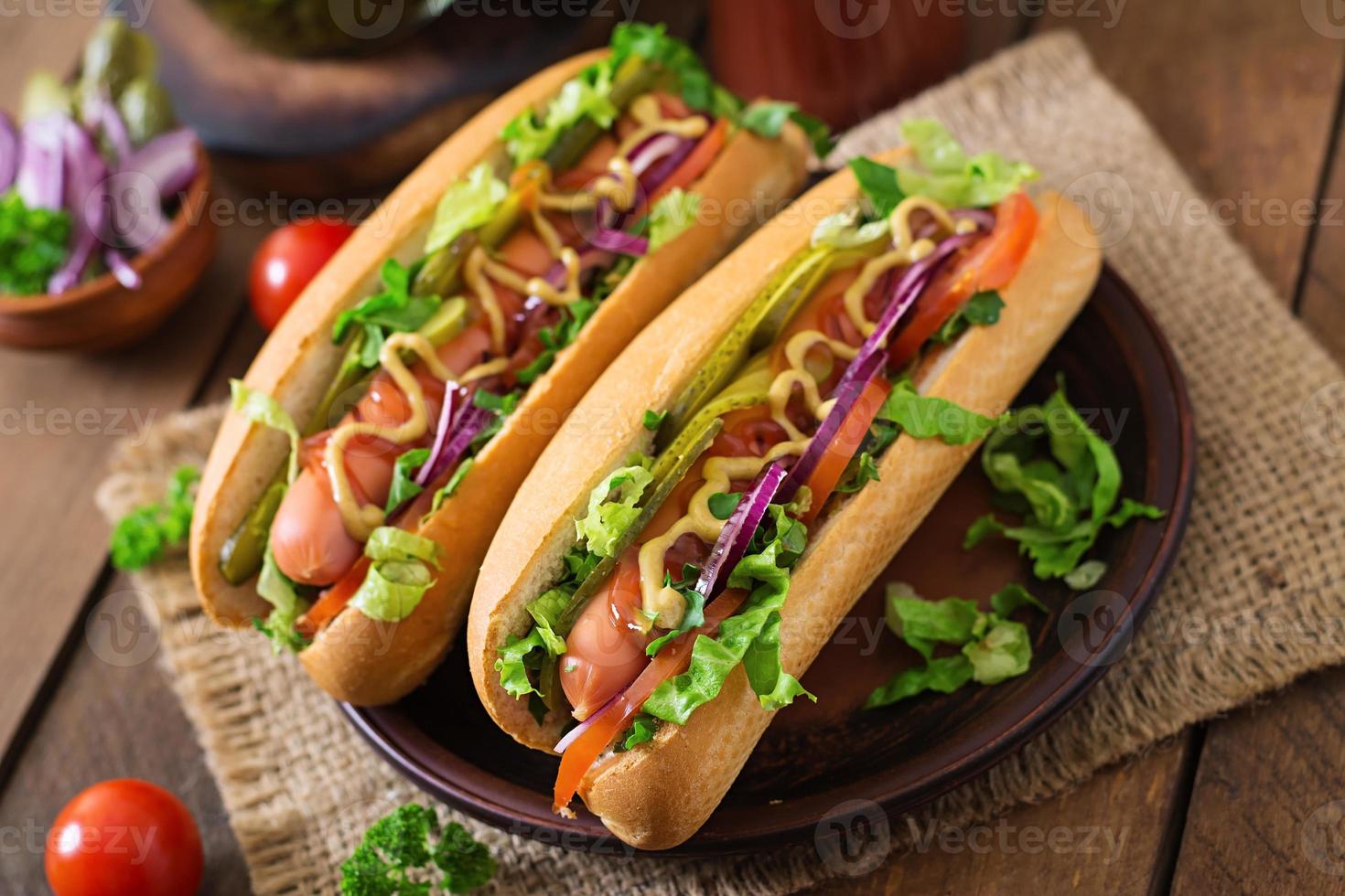 Hot dog with  pickles, tomato and lettuce on wooden background photo