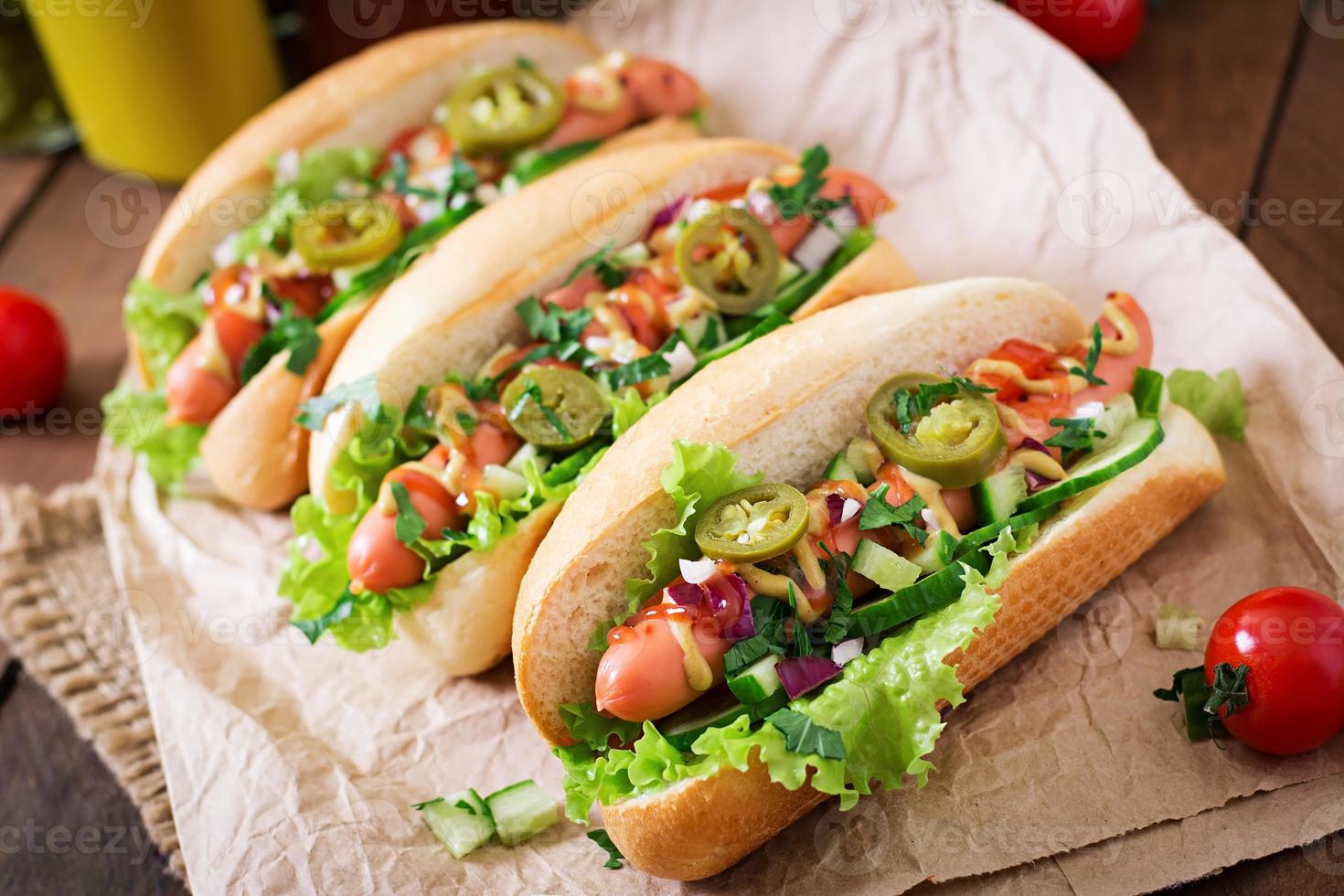 Hot dog with jalapeno peppers, tomato, cucumber and lettuce on wooden background photo
