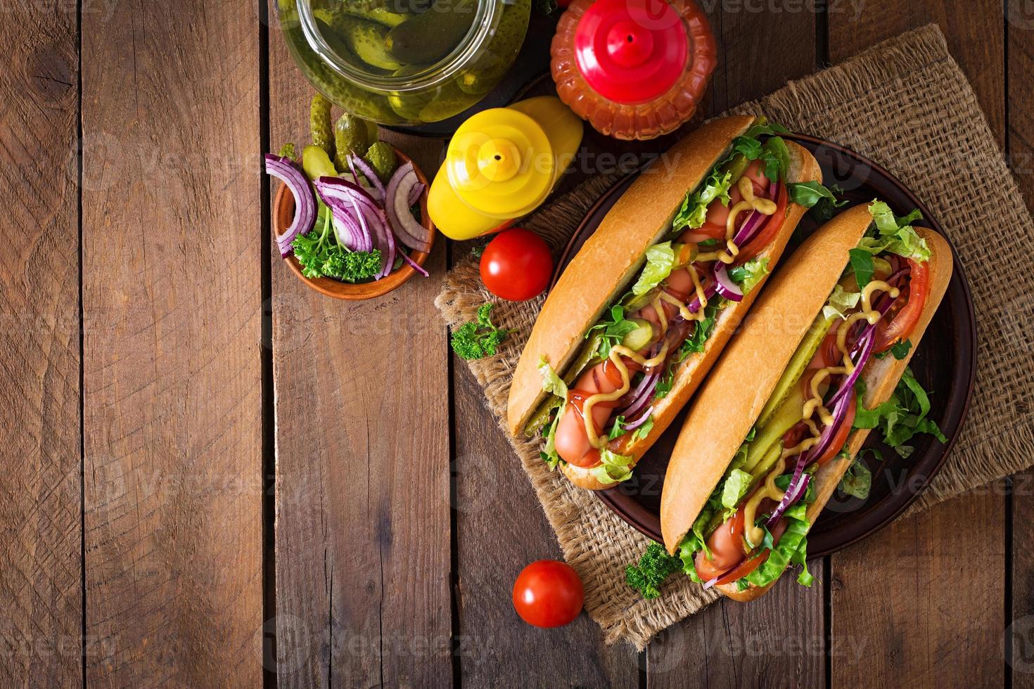 Hot dog with  pickles, tomato and lettuce on wooden background photo