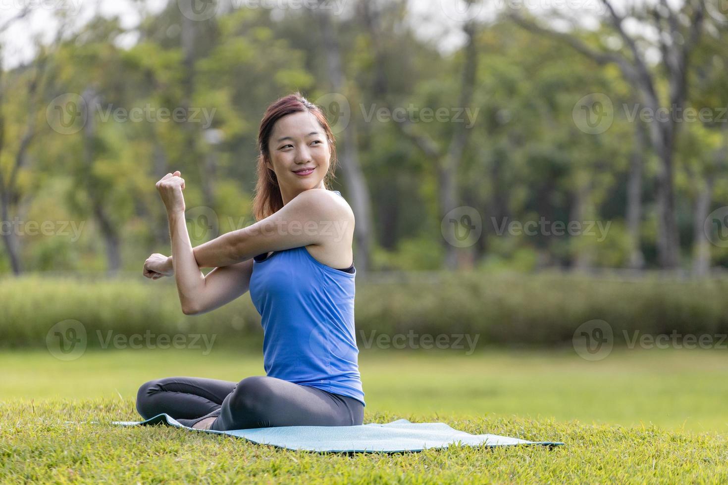Asian woman relaxingly practicing arm and shoulder stretching yoga inside the public park for cool down after exercise in the public park photo