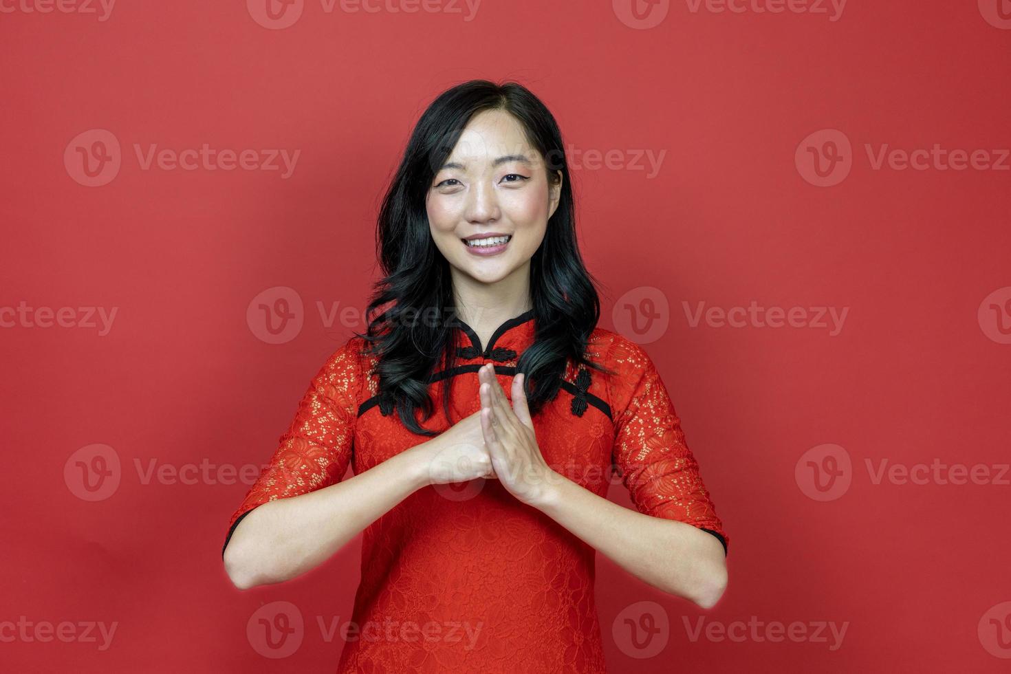 mujer china asiática en cheongsam rojo o qipao haciendo un gesto educado y respetuoso por desear buena suerte y prosperidad en la celebración del año nuevo chino aislada en un fondo rojo foto