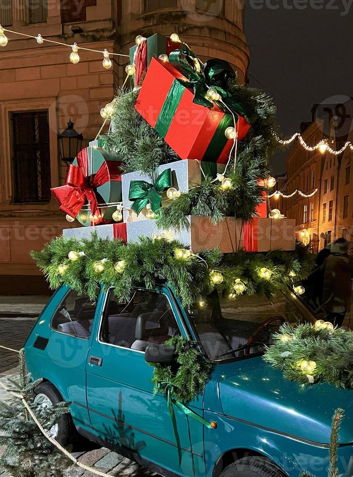 Santa's old vintage car with gift boxes on top. Closeup branches of coniferous tree decorated shiny light garland. Perfect festive content for stories background, vertical banner. photo