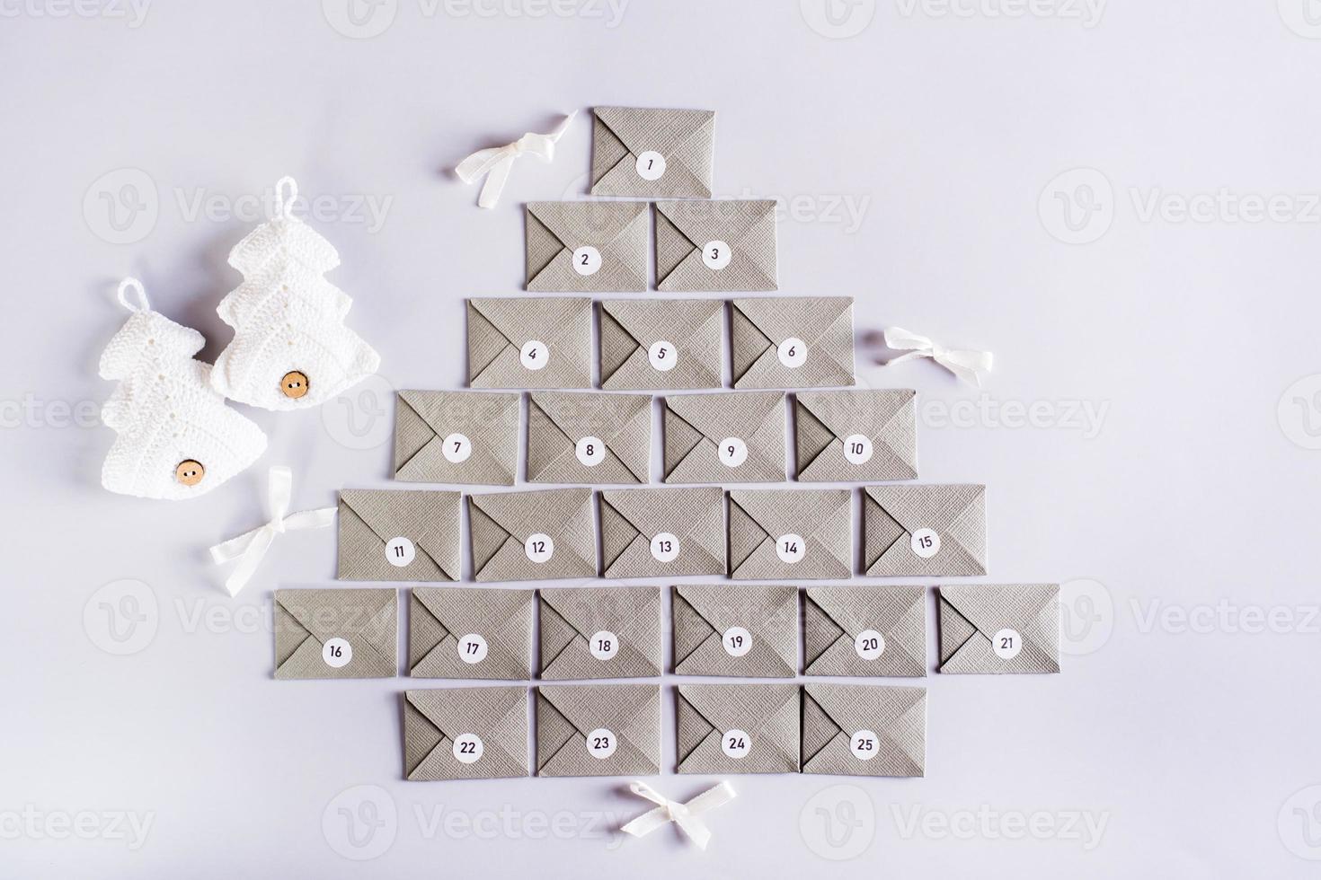 Envelopes for the advent calendar in the form of a Christmas tree and knitted fir trees on a gray photo