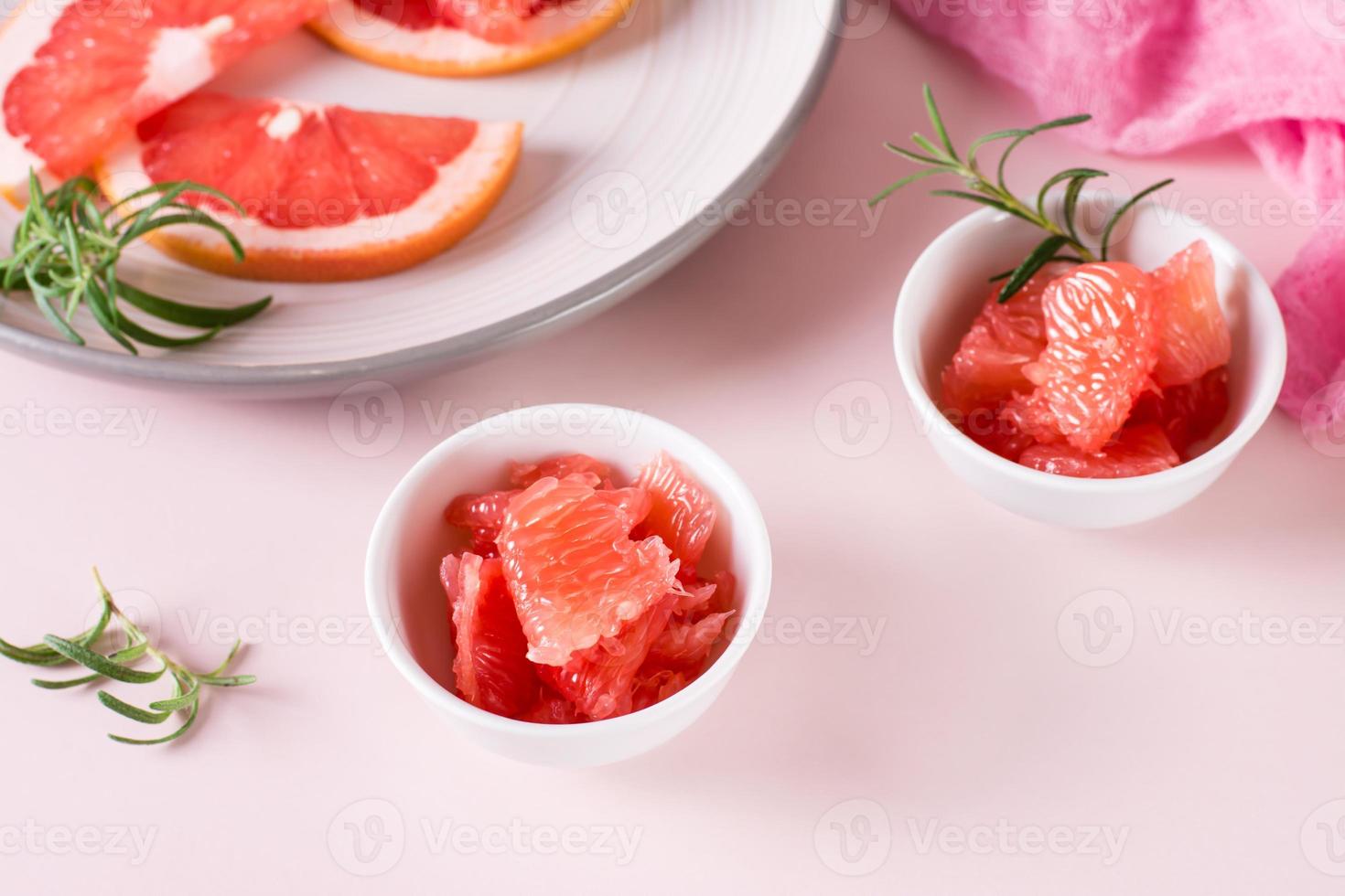 Juicy grapefruit slices and rosemary in a bowl on the table. Cocktail ingredients. photo