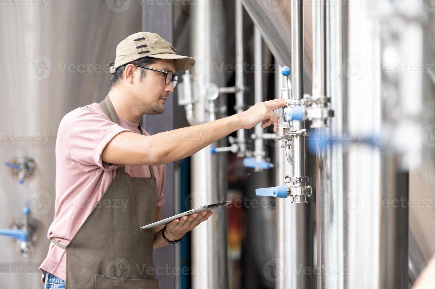 Young Asian worker inspecting brewery quality with a glass of craft beer evaluating visual appearance after preparation while working in a processing craft brewery. photo
