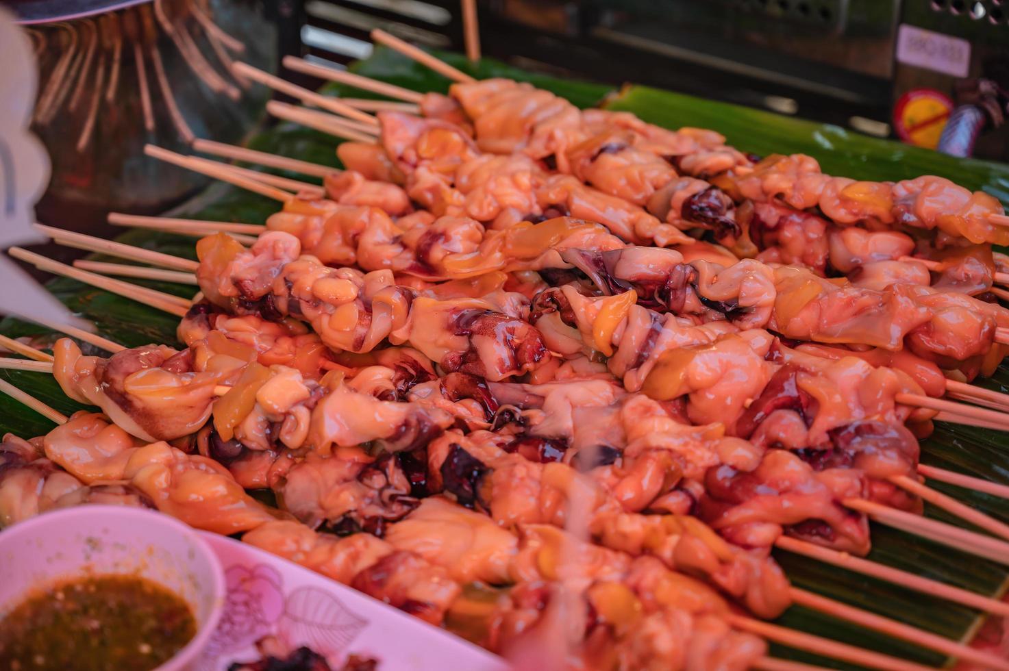 Close up raw squid meat skewer on banana leaf in the fresh market of thailand with spicy seafood sauce.Thailand street food photo