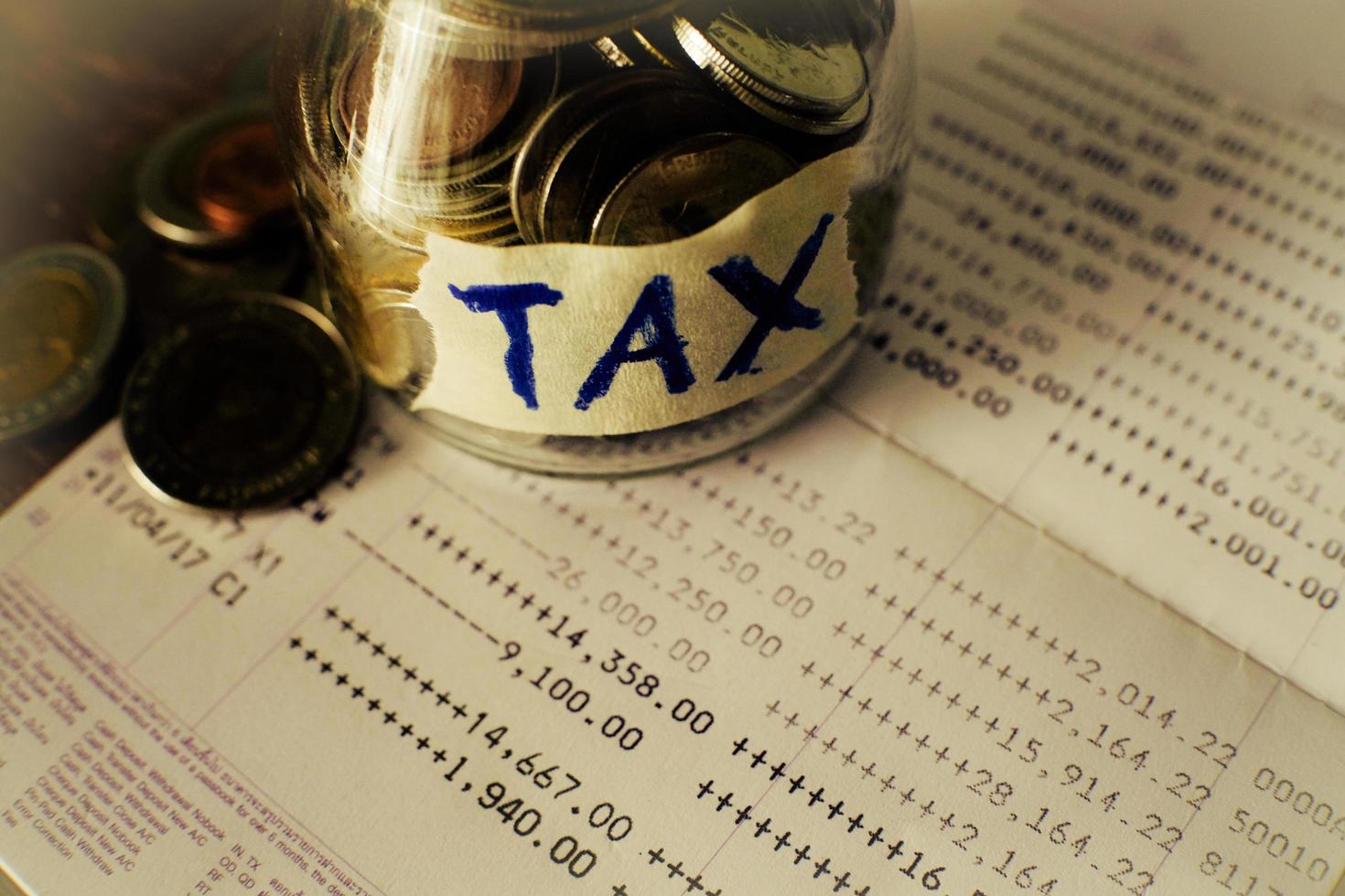 The glass jar full with the coins with TAX word on saving account passbook background. Financial and tax concept. Thai bath money in a jar. photo