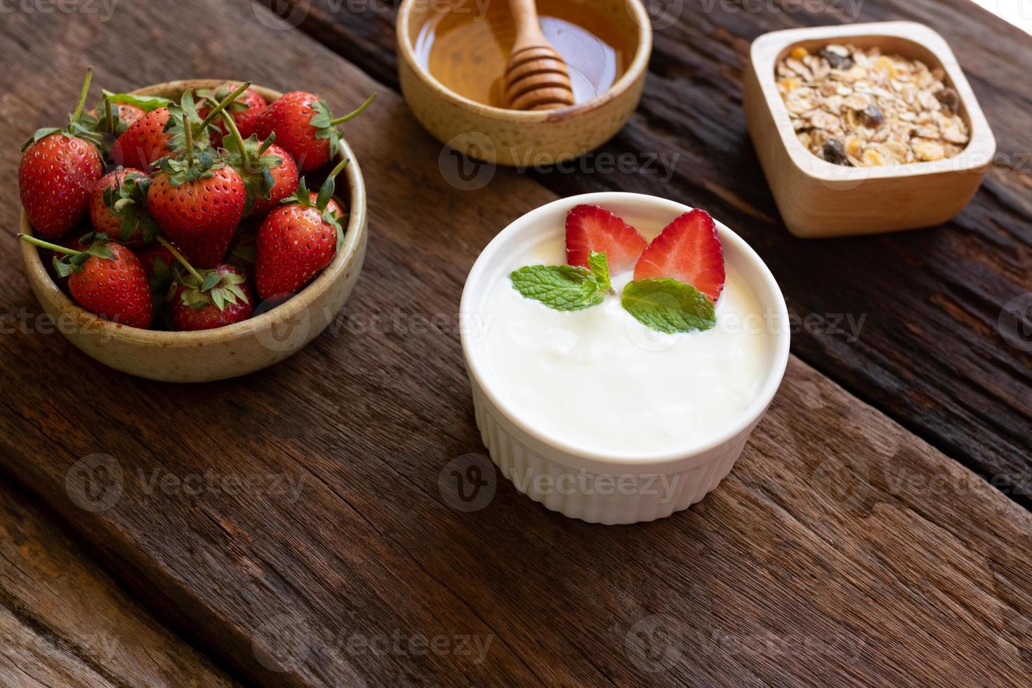 Strawberry yogurt in a wooden bowl with granola, honey, mint and fresh strawberry on wooden background. Health food concept. photo