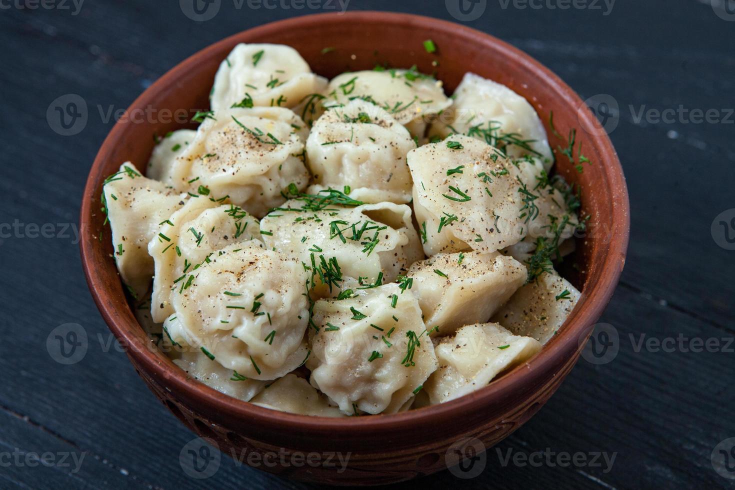 Traditional russian pelmeni or ravioli, dumplings with meat on wood black background. Russian food and russian kitchen concept. photo