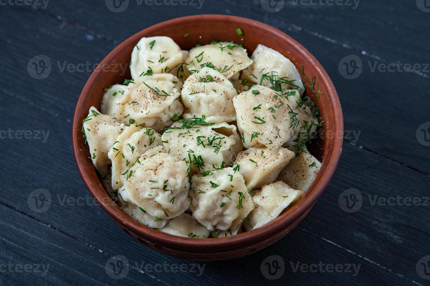 Traditional russian pelmeni or ravioli, dumplings with meat on wood black background. Russian food and russian kitchen concept. photo