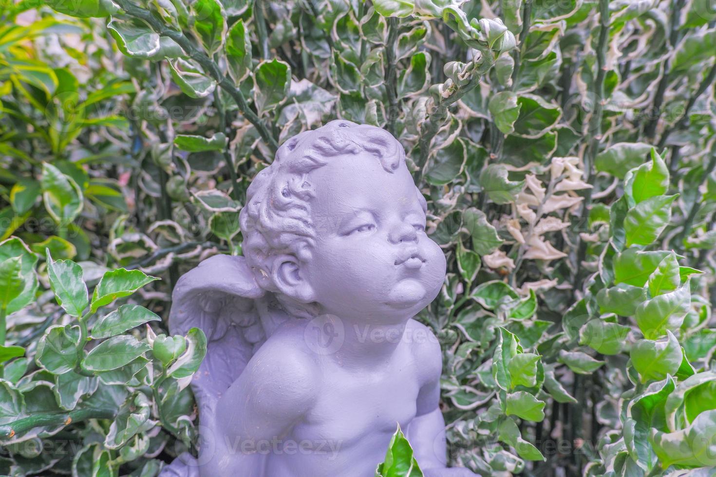 gray winged child statue set among green leaves. photo