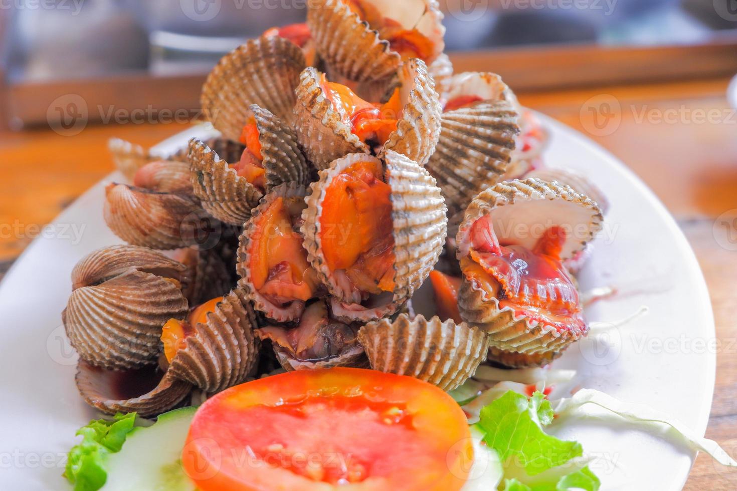 Steamed cockles boiled cockles are placed on a white plate. Garnished with sliced tomatoes. photo