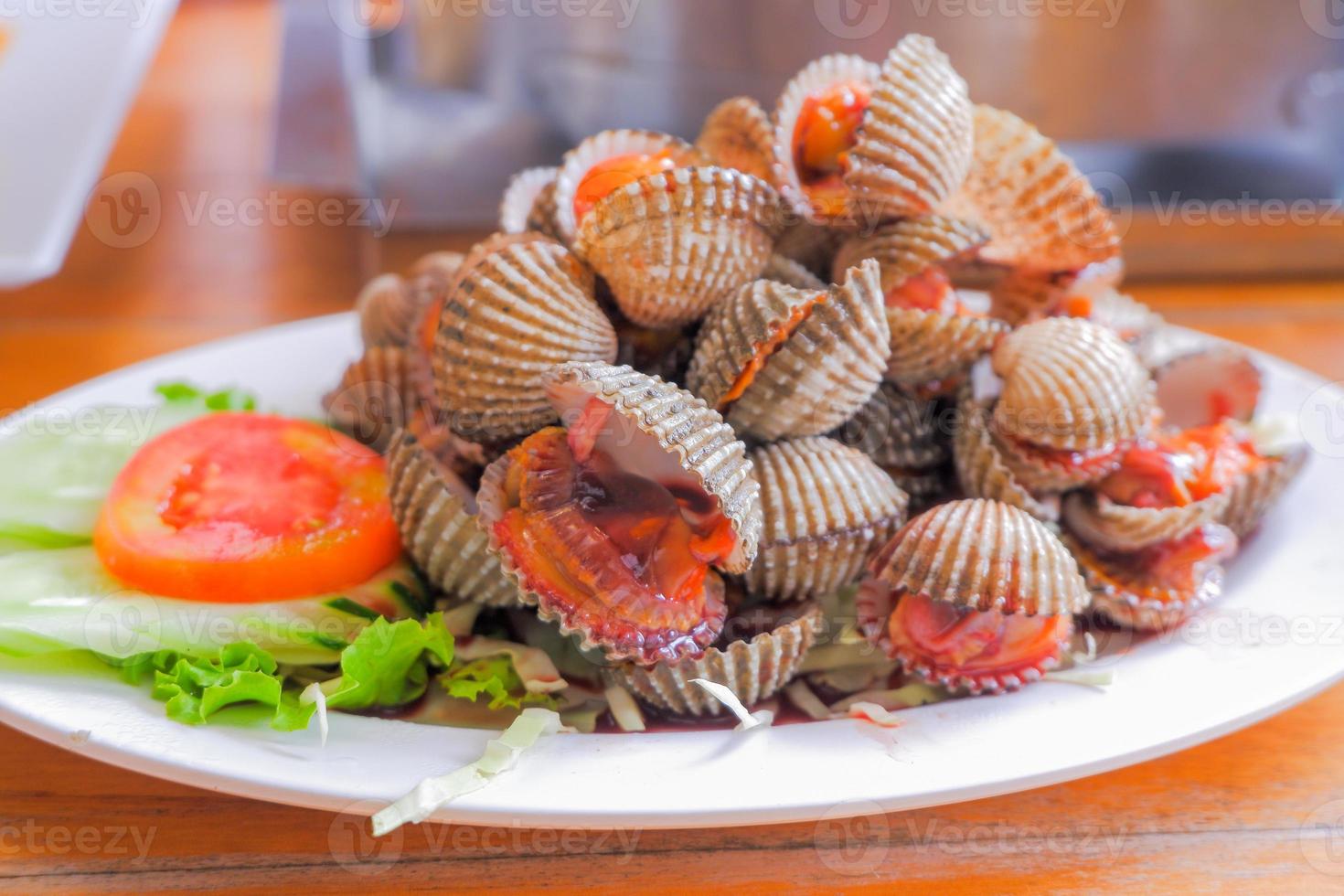 Steamed cockles boiled cockles are placed on a white plate. Garnished with sliced tomatoes. photo