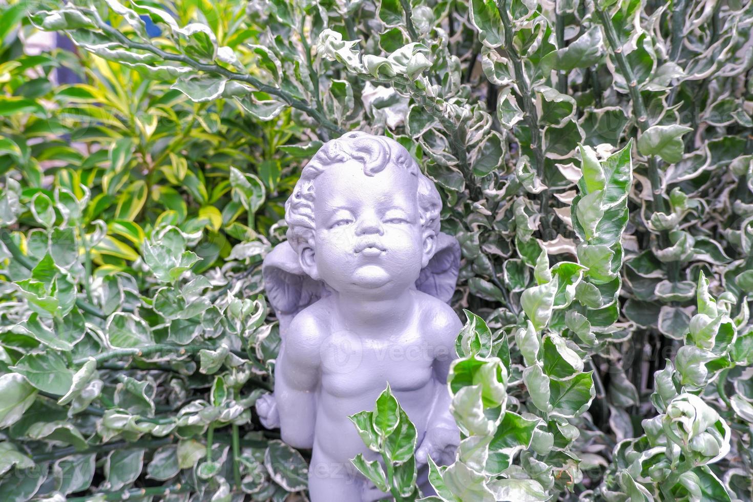 gray winged child statue set among green leaves. photo