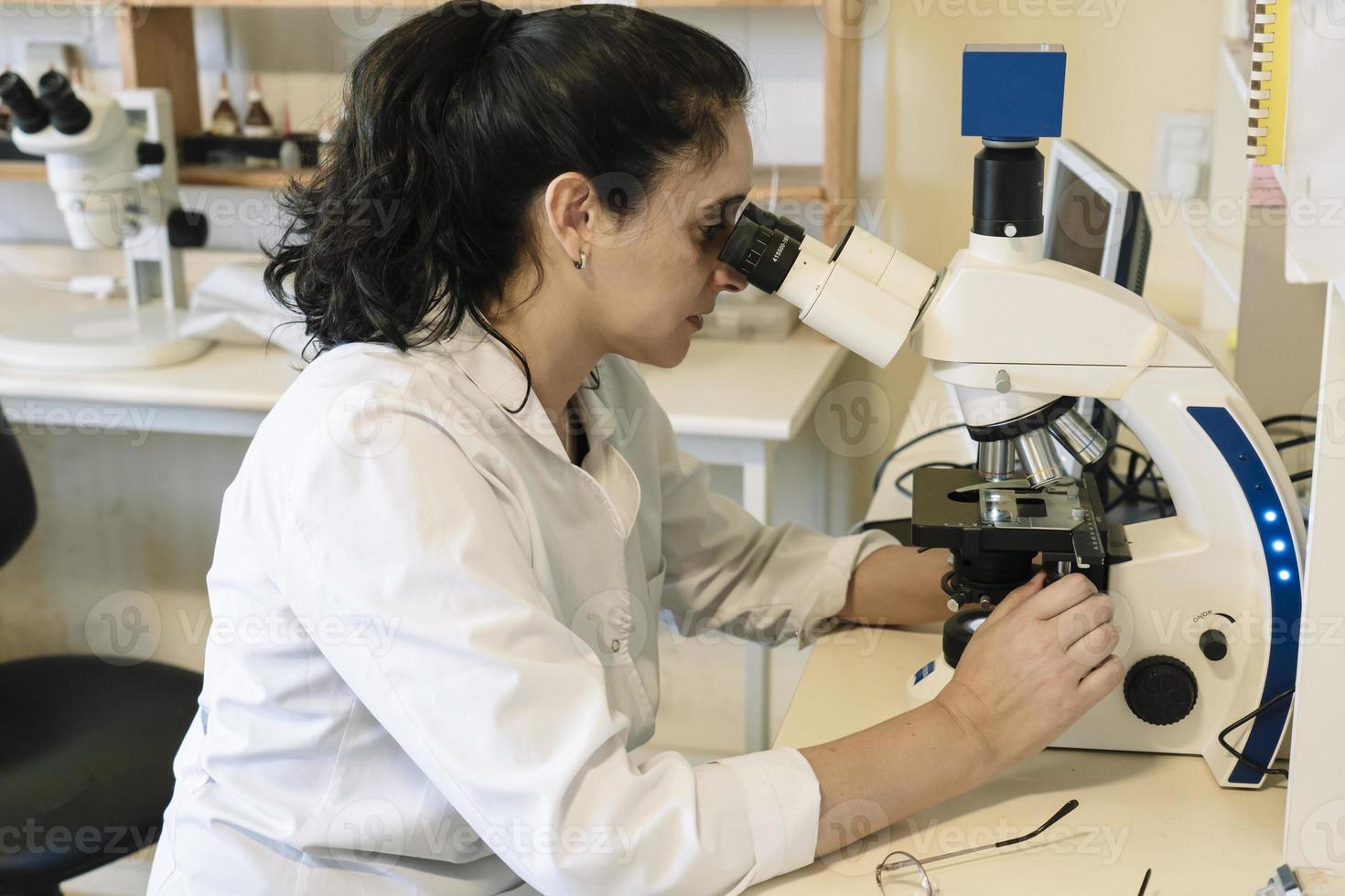 Female lab technician analyzing sample through microscope photo