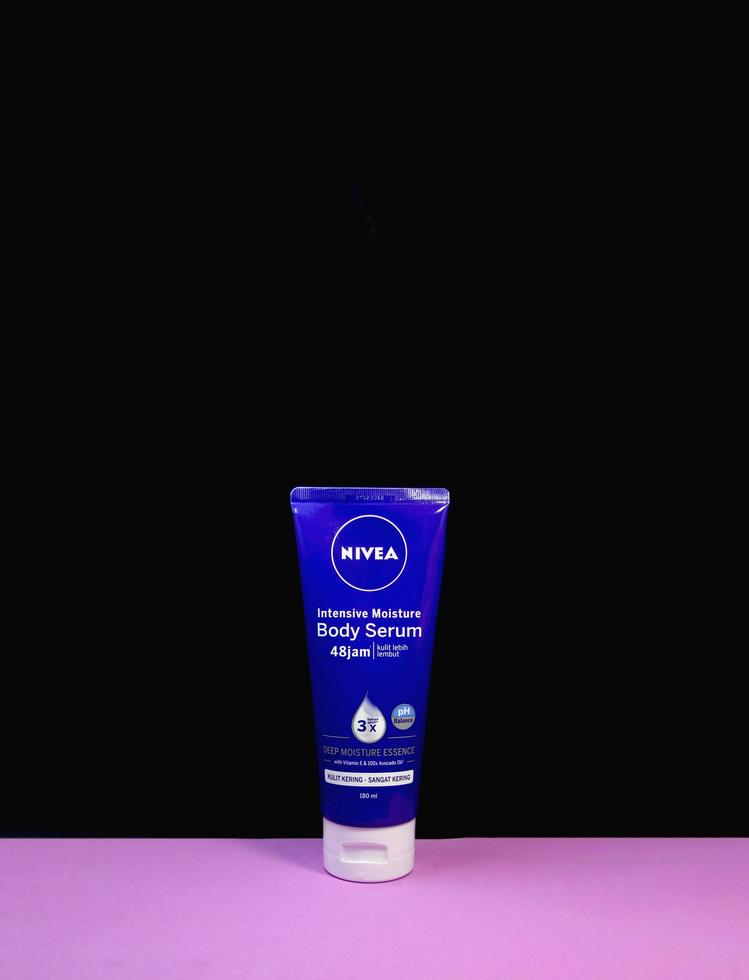 Central Jakarta, Indonesia - December 13th, 2022 - Nivea intensive blue body serum for sensitive screen isolated on pinkish purple and black colored vertical background with a lot of copy space. photo