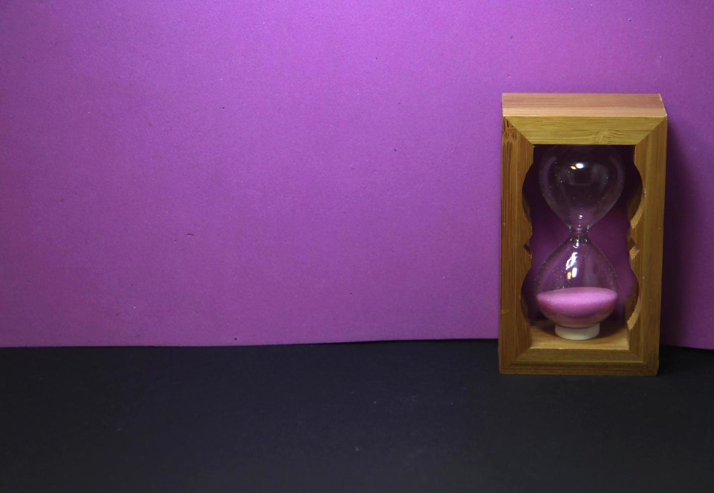 Wooden pink sand hourglass. Small sand glass photo decoration isolated on purple and black background. No text with space for copy space.