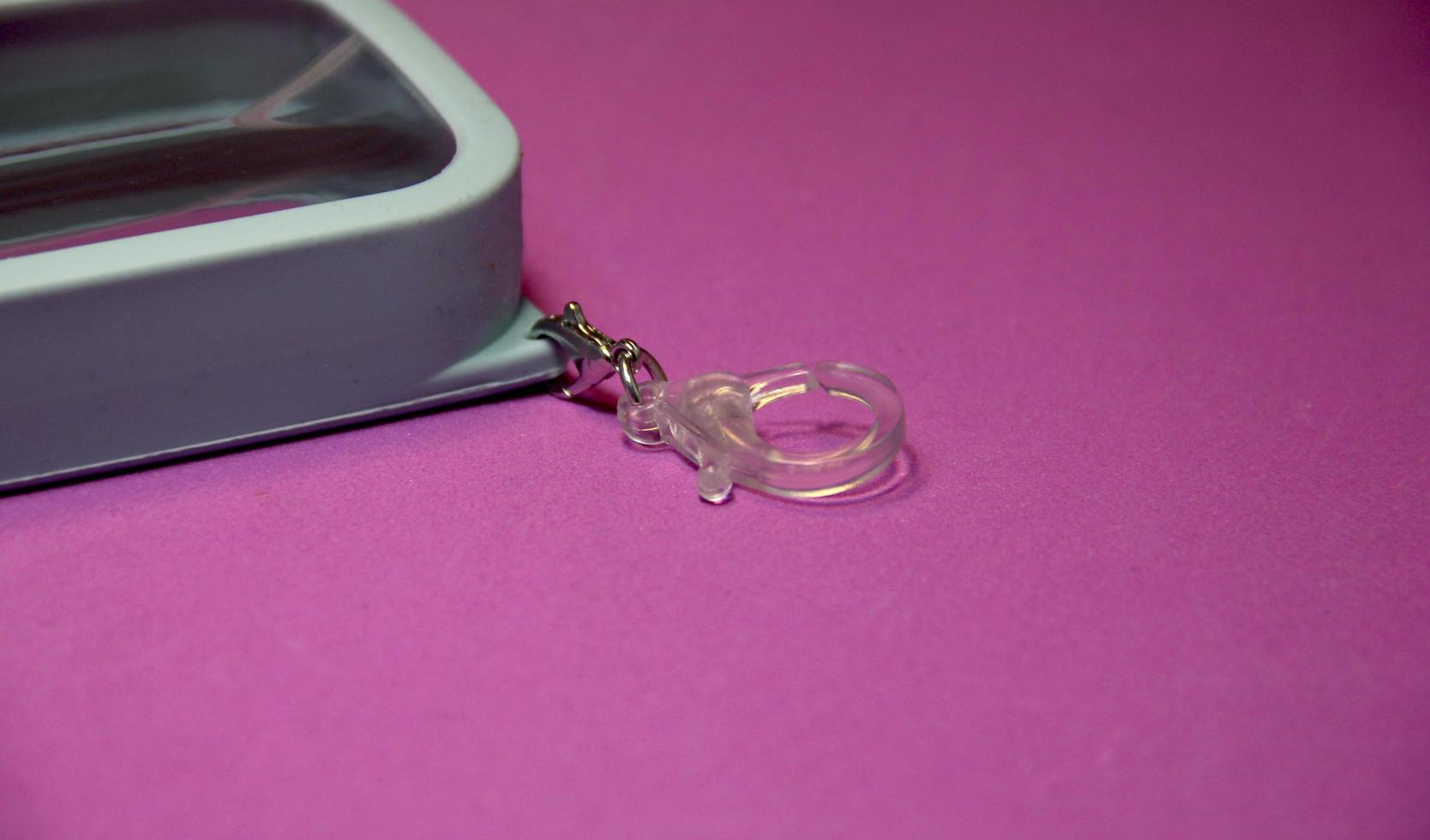 Transparent small object hook ring isolated on pinkish purple colored background for carrying portable hand sanitizer. photo