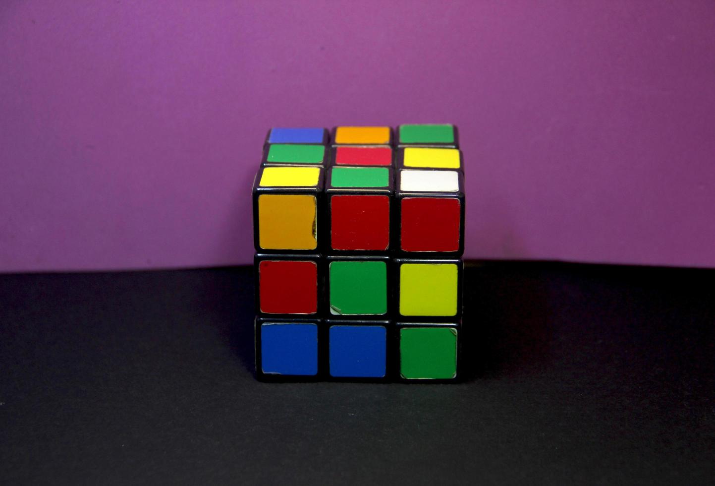 Unsolved rubik cube game for training the brain. Fun educational logic training photo isolated on purple and black surface background wallpaper.