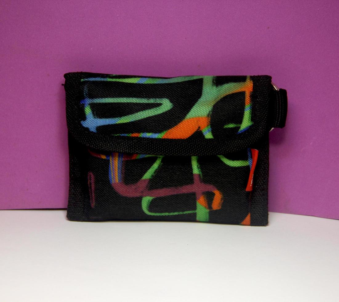 Black canvas fabric wallet with colorful doodle pattern for young or teen who love artsy things. Savings financial themed object photo isolated on white and purple background surface.