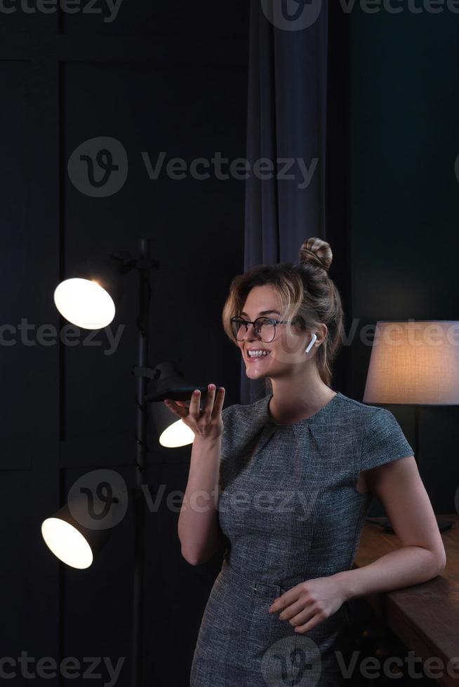 mujer de negocios que usa auriculares inalámbricos y teléfono inteligente durante el trabajo nocturno foto