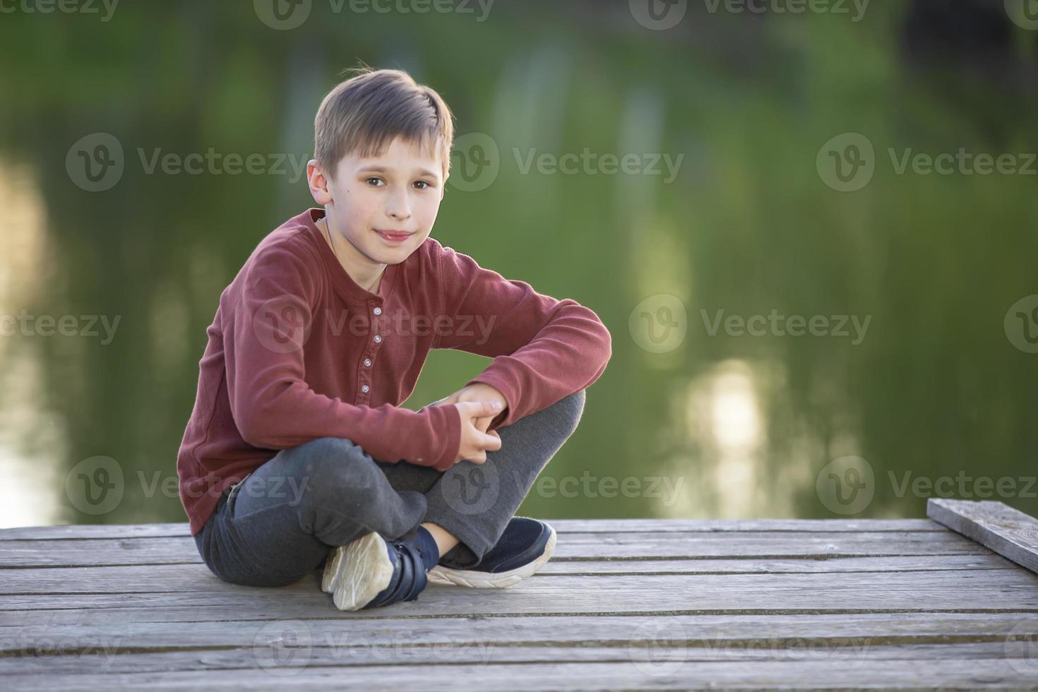 A handsome happy boy is sitting on a wooden bridge. photo