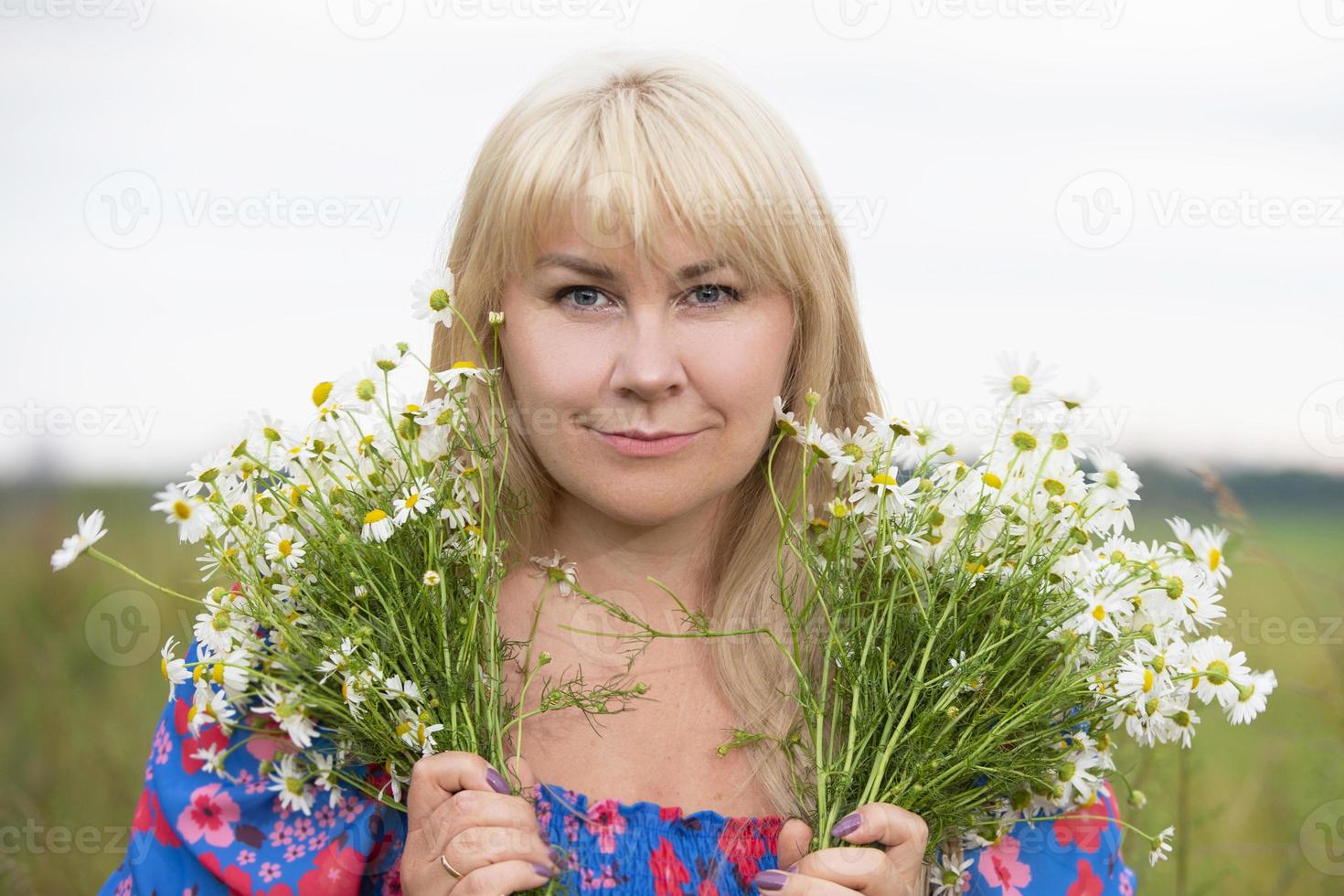 A beautiful plus size woman with white hair holds a bouquet of daisies, smiles, enjoys summer and life. photo