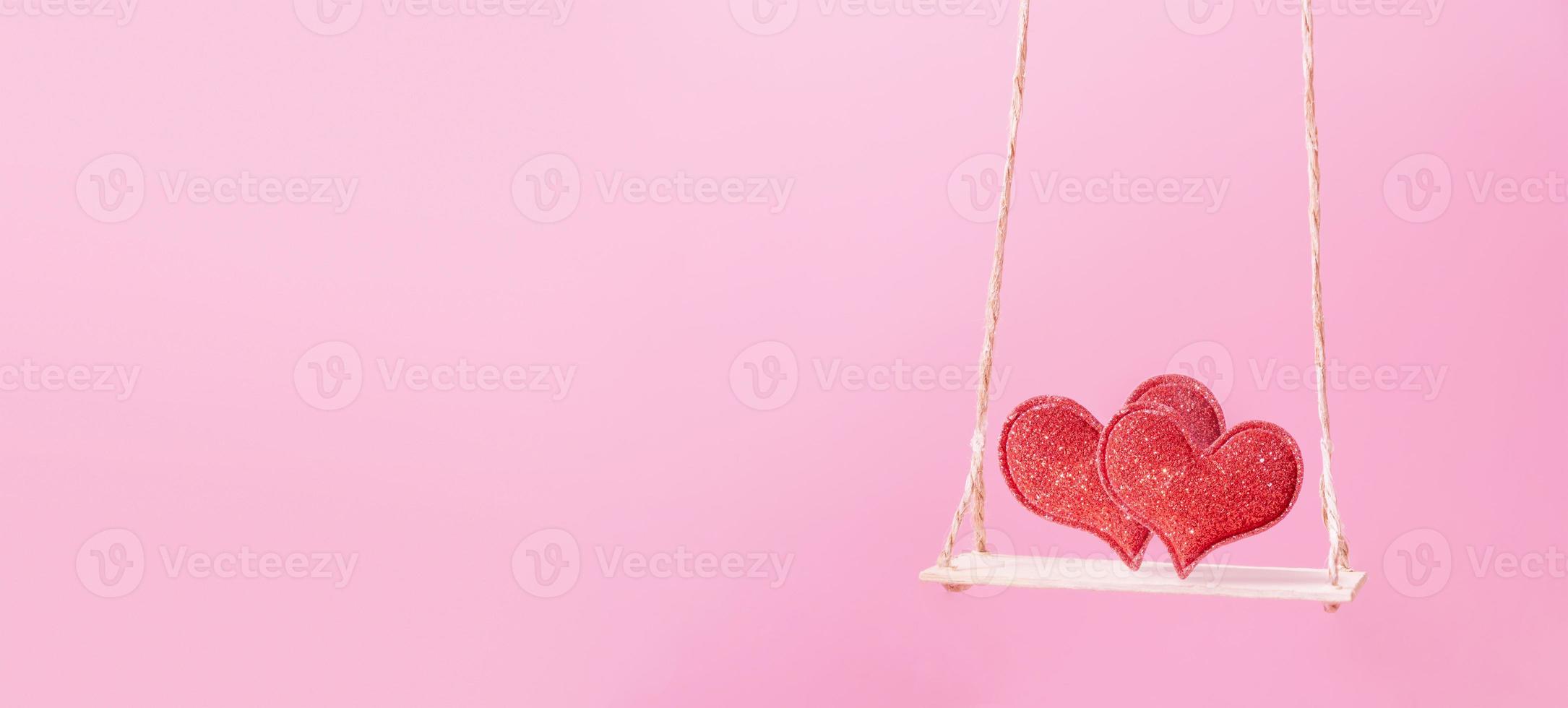 A swing with two hearts on pink background. Creative banner for 14 february. Copy space photo