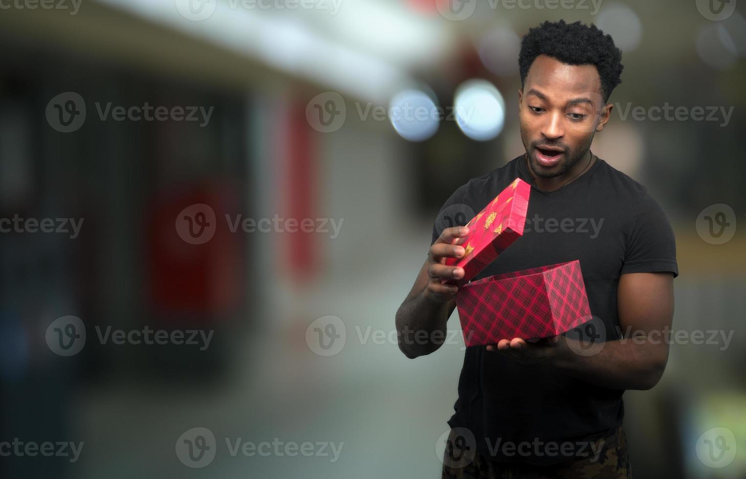 man opening box looking inside christmas gift surprise excited expression with mall bokeh light photo