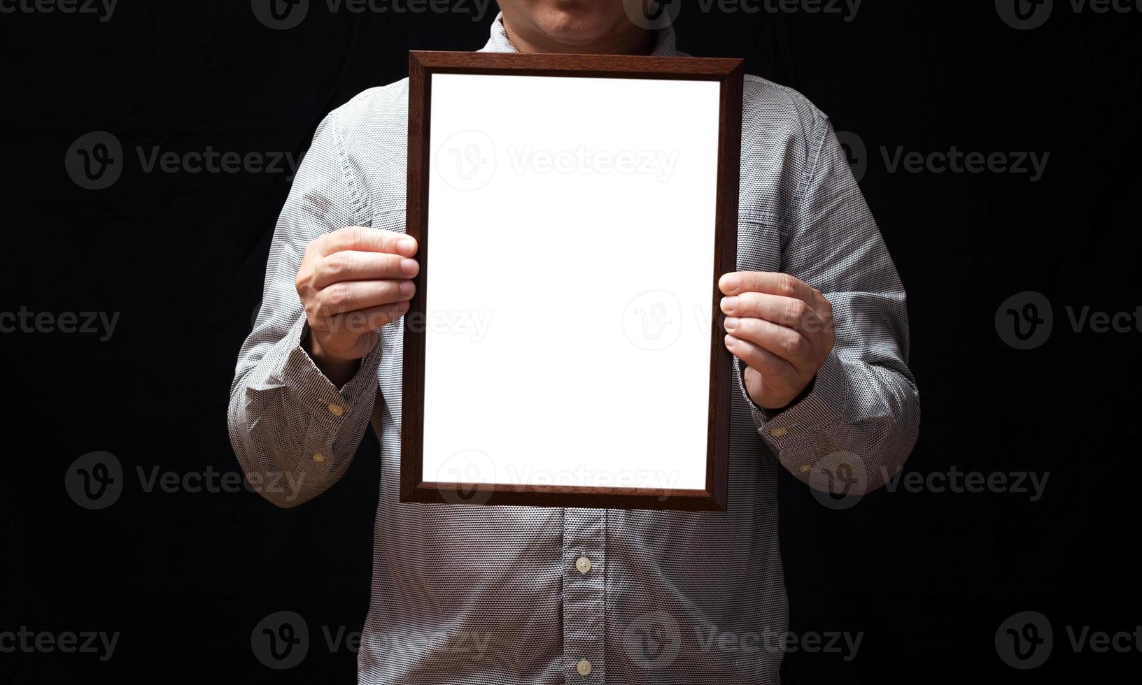 A blank diploma or a mockup certificate in the hand of a man employee wearing shirt on black background. The vertical picture frame is empty and the copy space. photo