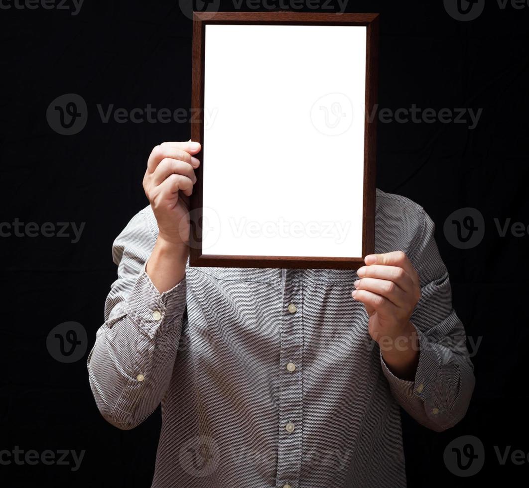 A blank diploma or a mockup certificate in the hand of a man employee wearing shirt on black background. The vertical picture frame is empty and the copy space. photo