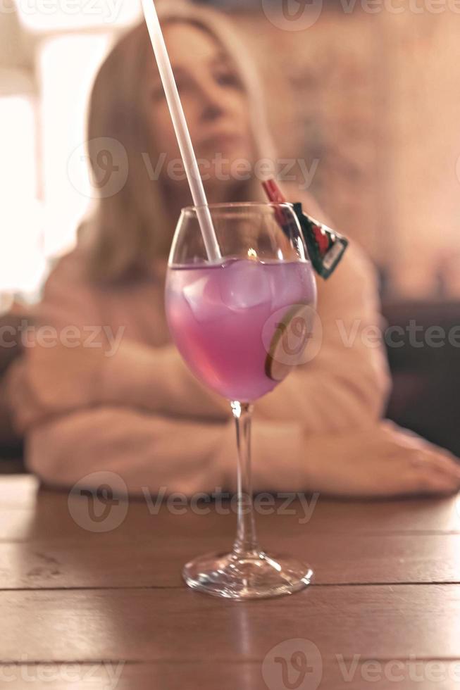 Fruity pink cocktail with a slice of lime on a table in a cafe. In the background, a blurry figure of a woman sitting at a table photo