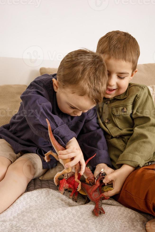 Two little and cute caucasian boys playing with dinosaurs at home. Interior and clothes in natural earth colors. Cozy environment. Children having fun with toys, two friends. photo