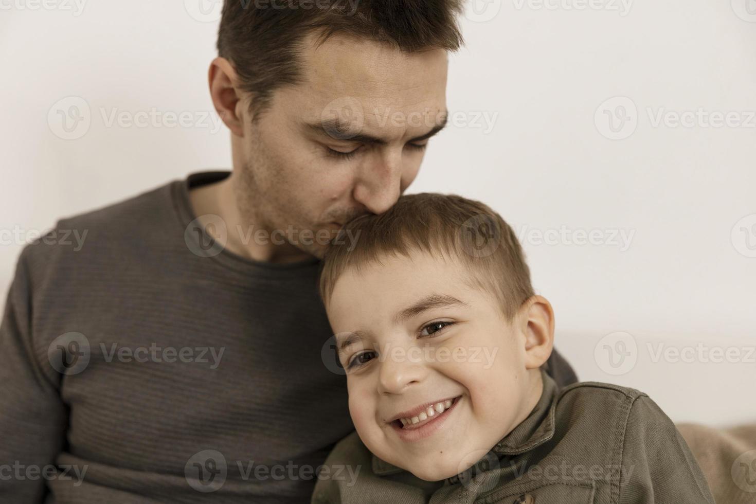 padre besando a su hijo. papá ama a su hijo. un joven atractivo y un niño caucásico se divierten juntos. interior y ropa en colores tierra naturales. ambiente acogedor. foto