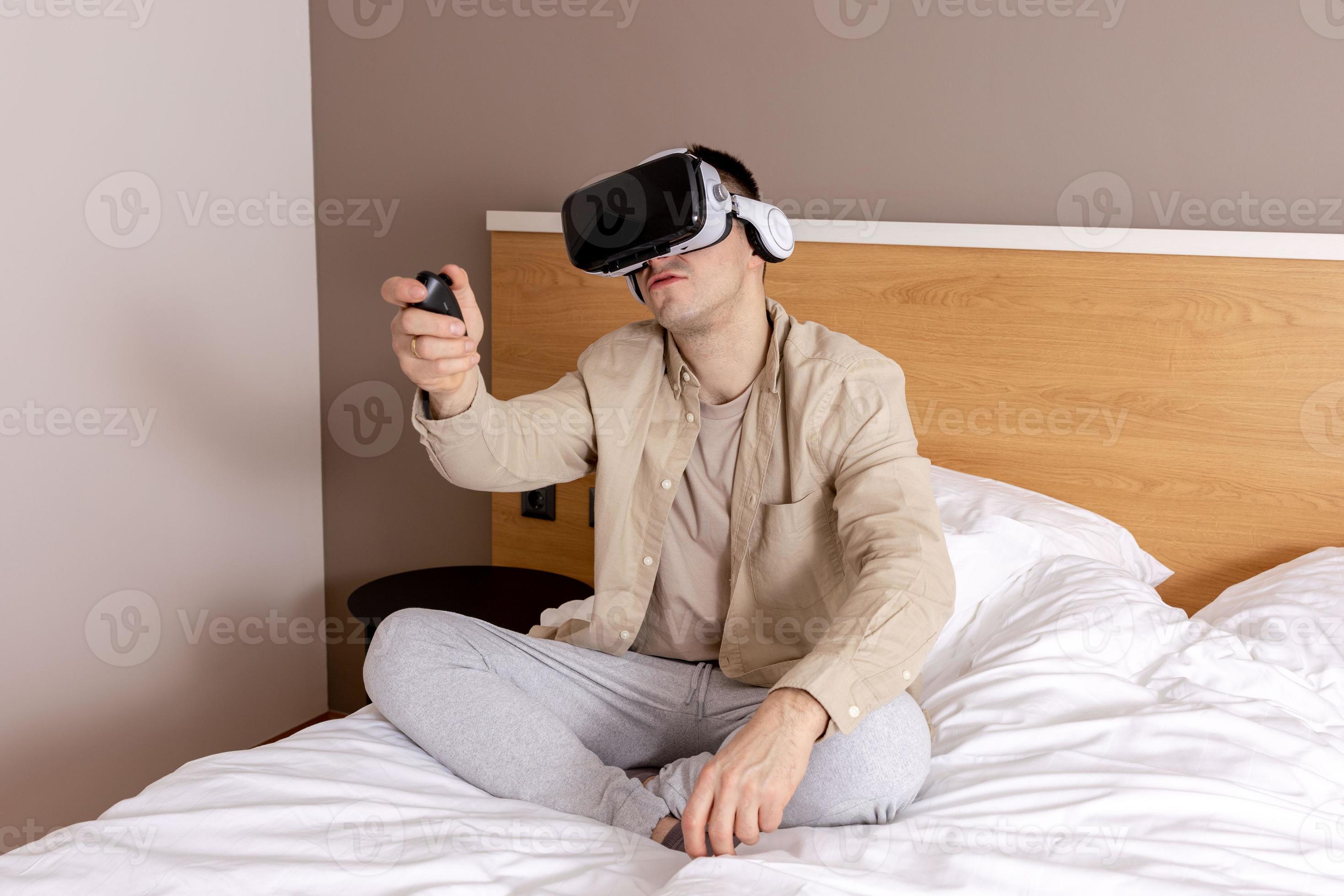 joven caucásico sentado en la cama en casa con auriculares vr y jugando  videojuegos interactivos, explorando la realidad virtual. hombre con gafas  vr. futuro, gadgets, tecnología, educación, estudio en línea. 15939391 Foto