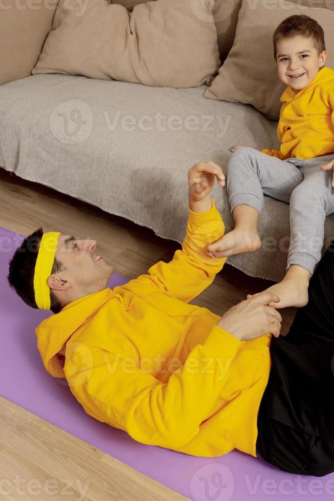 joven con niño pequeño haciendo ejercicios de fitness en casa. padre e hijo divirtiéndose durante el deporte. papá y su hijo haciendo entrenamiento. deporte, yoga. hacer ejercicio en el apartamento. estilo de vida saludable, familia. foto