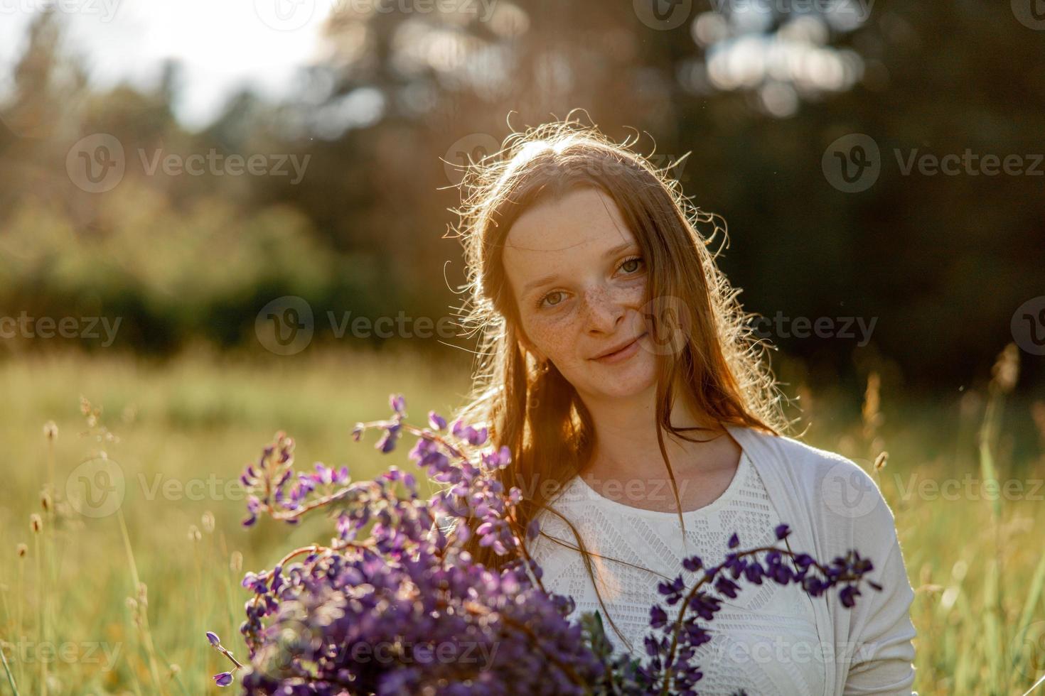 Close up portrait of young beautiful redhead woman with freckles, wearing white dress, posing in the nature. Girl with red hair holding flowers. Natural beauty. Diversity, individual uniqueness. photo